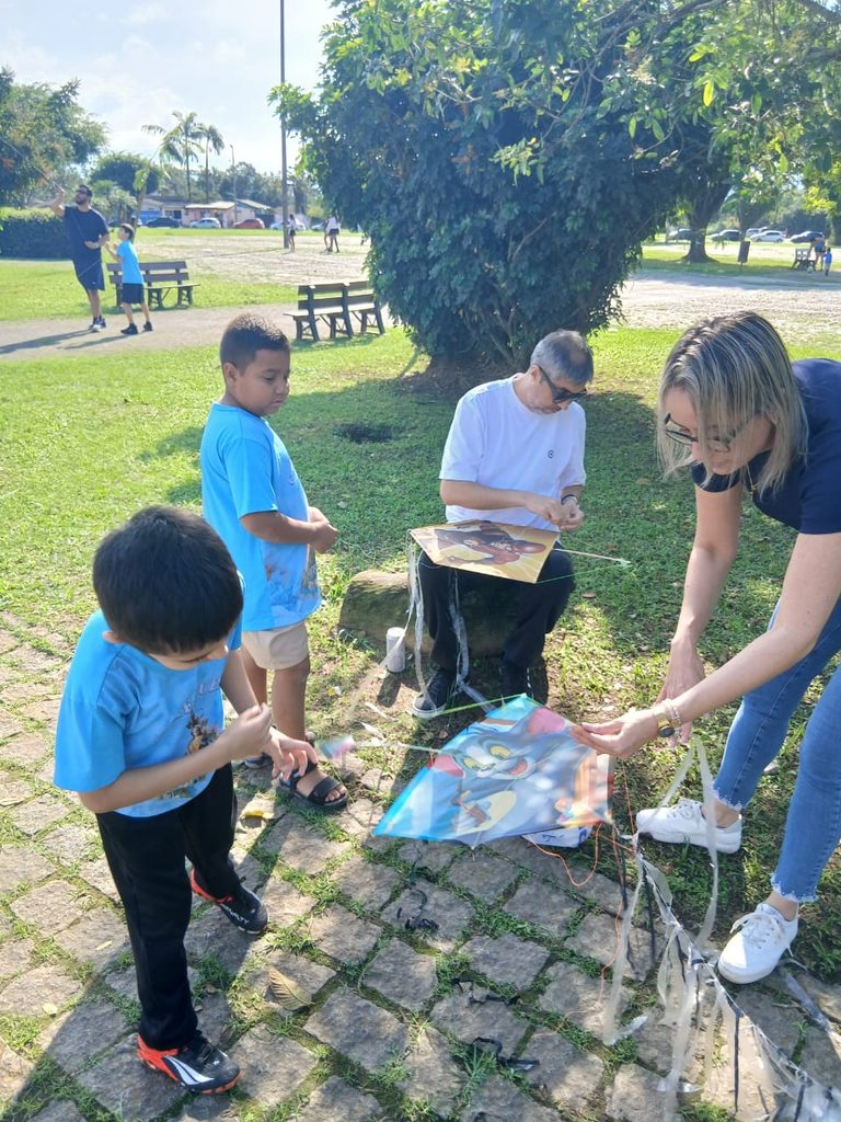  Pai e filho ajustando a linha de uma pipa durante evento de integração da Catequese do Santuário.
