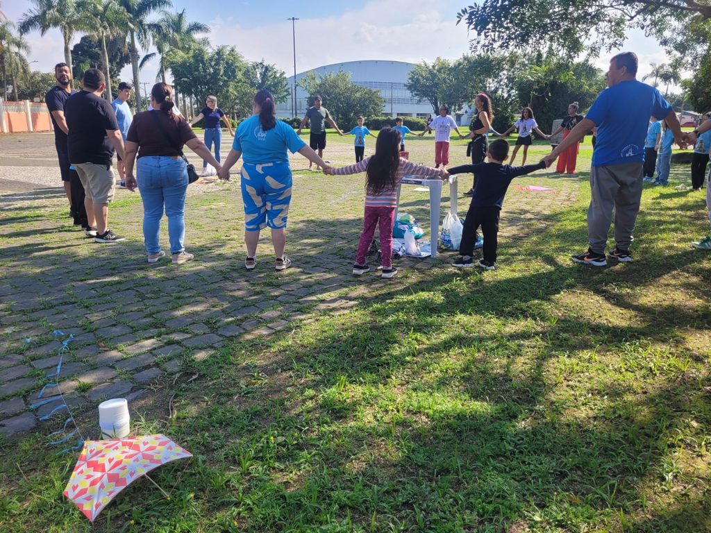 Famílias da Catequese em círculo fazendo oração ao ar livre no gramado do Santuário.