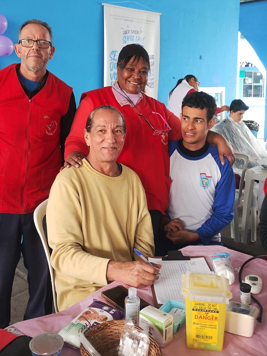 Sula, coordenadora da Pastoral da AIDS, reunida com a equipe de voluntários. Eles estão juntos, transmitindo união e sentimento de missão cumprida após os atendimentos sociais em Paranaguá.